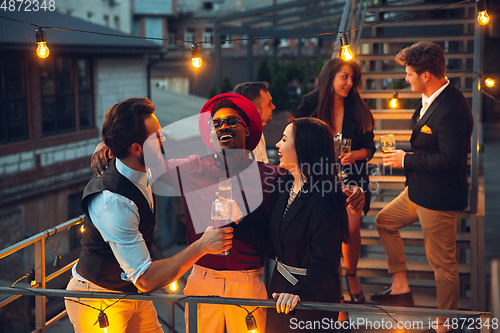 Image of Corporate celebrating in the warm light of the lamps in summer evening, young friends, colleagues look happy, talk, have fun