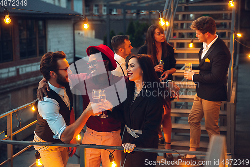 Image of Corporate celebrating in the warm light of the lamps in summer evening, young friends, colleagues look happy, talk, have fun