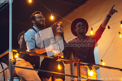 Image of Corporate celebrating in the warm light of the lamps in summer evening, young friends, colleagues look happy, talk, have fun