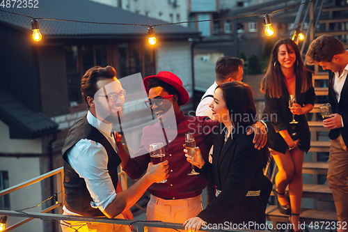 Image of Corporate celebrating in the warm light of the lamps in summer evening, young friends, colleagues look happy, talk, have fun