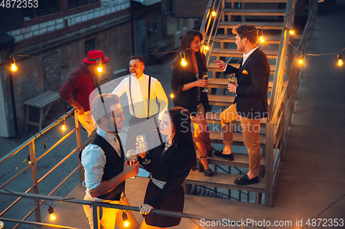 Image of Corporate celebrating in the warm light of the lamps in summer evening, young friends, colleagues look happy, talk, have fun