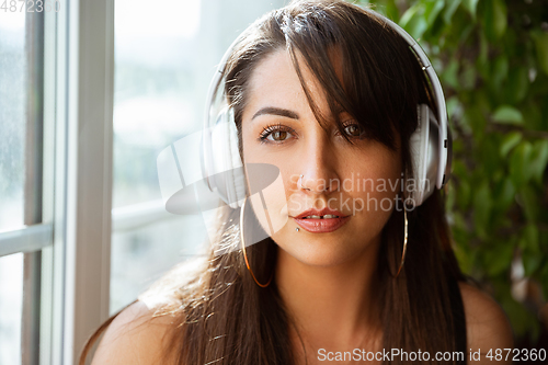Image of Close up of beautiful caucasian woman in wireless headphones listening to music, calm and attractive