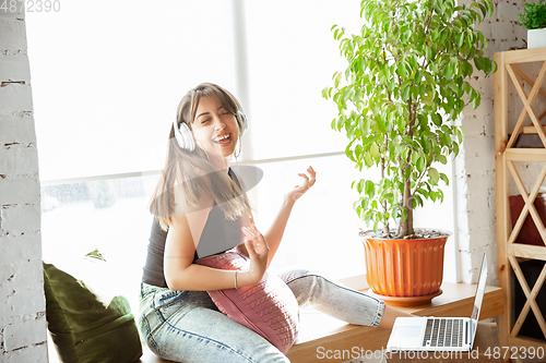 Image of Caucasian female singer during online concert at home insulated and quarantined, cheerful and happy, singing live, performing