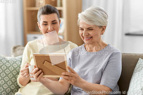 Image of adult daughter and old mother with photo at home