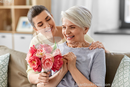 Image of adult daughter giving flowers to old mother