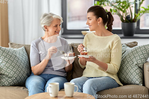 Image of old mother and adult daughter eating cake at home