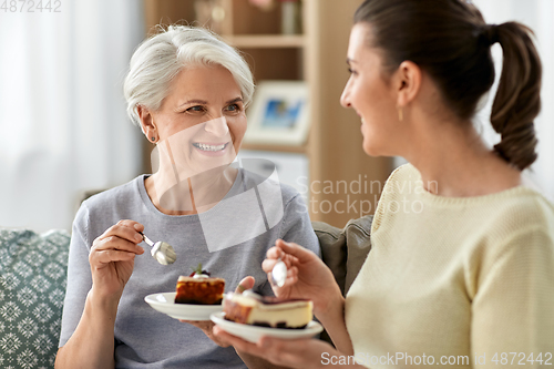 Image of old mother and adult daughter eating cake at home