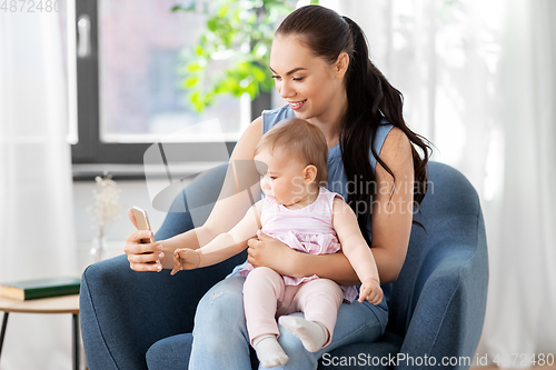 Image of happy mother and baby with smartphone at home