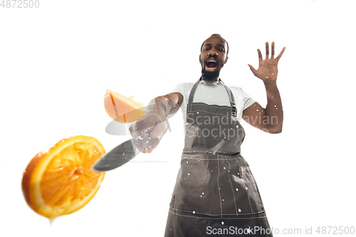 Image of Amazing african-american man preparing unbelievable food with close up action, details and bright emotions, professional cook. Cutting orange on the fly