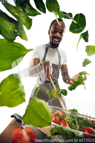 Image of Amazing african-american man preparing unbelievable food with close up action, details and bright emotions, professional cook. Adding salad greens on the fly