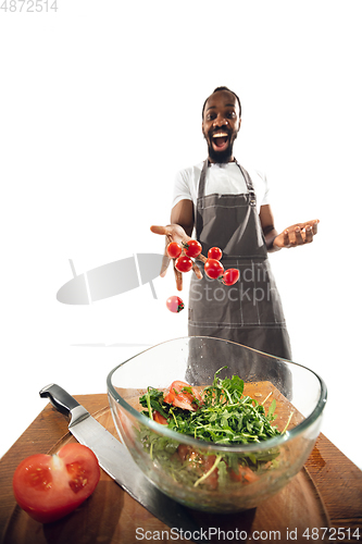 Image of Amazing african-american man preparing unbelievable food with close up action, details and bright emotions, professional cook. Adding cherry tomatos to salad on the fly