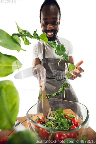 Image of Amazing african-american man preparing unbelievable food with close up action, details and bright emotions, professional cook. Adding salad greens on the fly