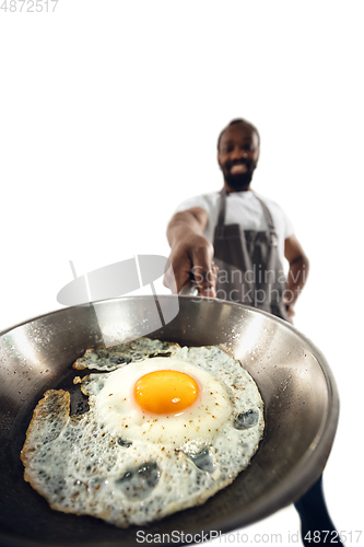 Image of Amazing african-american man preparing unbelievable food with close up action, details and bright emotions, professional cook. Preparing fried eggs