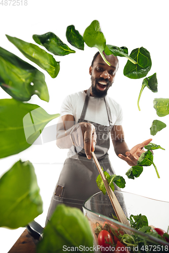 Image of Amazing african-american man preparing unbelievable food with close up action, details and bright emotions, professional cook. Adding salad greens on the fly