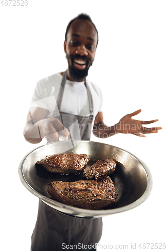 Image of Amazing african-american man preparing unbelievable food with close up action, details and bright emotions, professional cook. Preparing fried meat, steakes