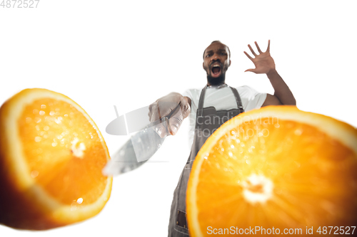 Image of Amazing african-american man preparing unbelievable food with close up action, details and bright emotions, professional cook. Cutting orange on the fly