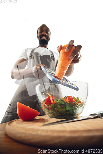 Image of Amazing african-american man preparing unbelievable food with close up action, details and bright emotions, professional cook. Cutting carrot to salad