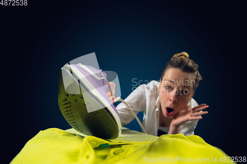 Image of Close up of young caucasian woman ironing bright clothes with expressive emotions in action, motion