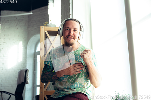 Image of Young man gesturing during a video conference in the living room. Attented listening