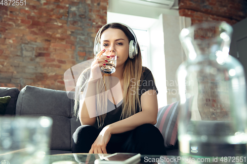 Image of Young woman wearing wireless headphones gesturing during a video conference in the living room. Attented listening