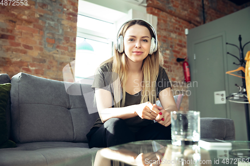 Image of Young woman wearing wireless headphones gesturing during a video conference in the living room. Attented listening