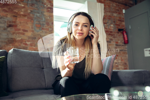 Image of Young woman wearing wireless headphones gesturing during a video conference in the living room. Attented listening