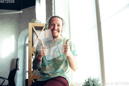 Image of Young man gesturing during a video conference in the living room. Thummb up, smiling