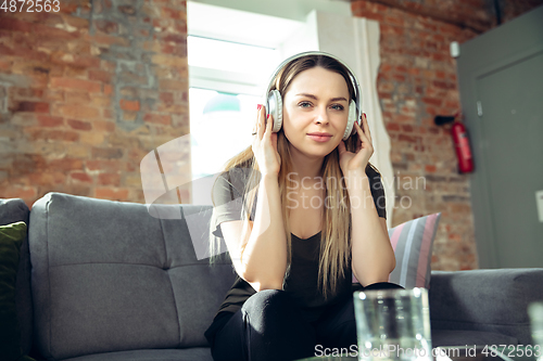 Image of Young woman wearing wireless headphones gesturing during a video conference in the living room. Attented listening