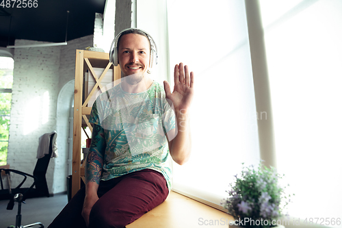 Image of Young man gesturing during a video conference in the living room. Waving, smiling