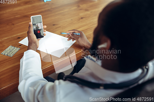 Image of Doctor advising the patient online with smartphone. African-american doctor during his videocall, work with patients, explaining recipes for drug, checking symptoms