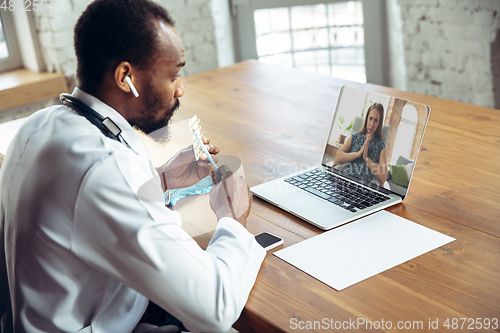 Image of Doctor advising the patient online with laptop. African-american doctor during his videocall, work with patients, explaining recipes for drug.