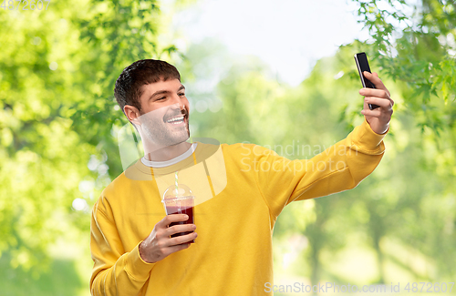Image of happy man with smartphone and juice taking selfie