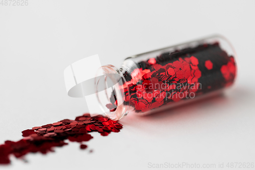 Image of red glitters poured from small glass bottle