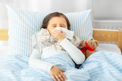 Image of sick girl lying in bed and blowing nose at home