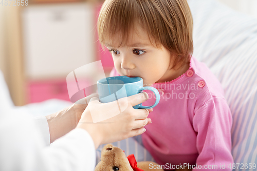 Image of doctor giving hot tea to sick little girl in bed