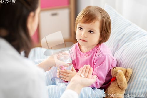 Image of doctor giving medicine to sick girl in bed at home