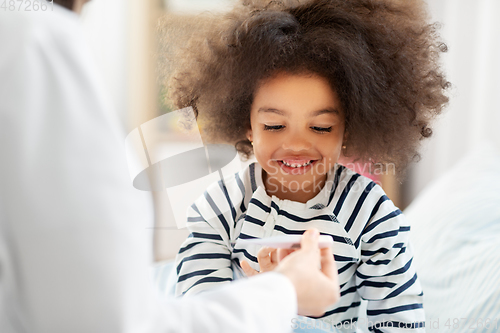 Image of doctor showing thermometer to smiling sick girl