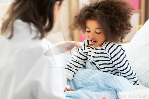 Image of doctor giving medicine to sick girl in bed at home