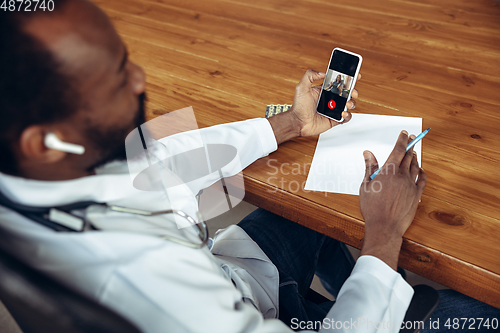 Image of Doctor advising the patient online with smartphone. African-american doctor during his videocall, work with patients, explaining recipes for drug, checking symptoms