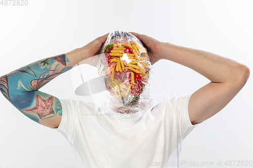 Image of Male face covered with oilcloth, cellophane and unhealthy food, hard to breathe. People lost their faces, can\'t notice the environmental pollution made by themself.