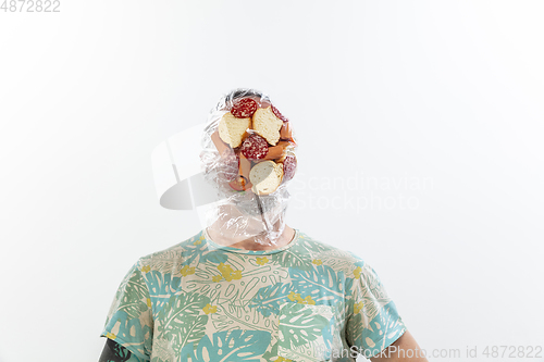 Image of Male face covered with oilcloth, cellophane and unhealthy food, hard to breathe. People lost their faces, can\'t notice the environmental pollution made by themself.