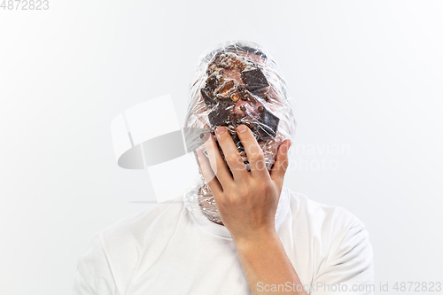 Image of Male face covered with oilcloth, cellophane and unhealthy food, hard to breathe. People lost their faces, can\'t notice the environmental pollution made by themself.