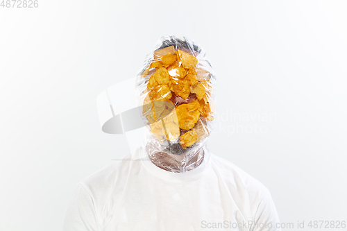 Image of Male face covered with oilcloth, cellophane and unhealthy food, hard to breathe. People lost their faces, can\'t notice the environmental pollution made by themself.