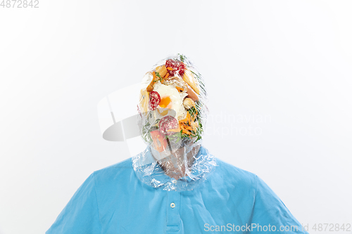 Image of Male face covered with oilcloth, cellophane and unhealthy food, hard to breathe. People lost their faces, can\'t notice the environmental pollution made by themself.