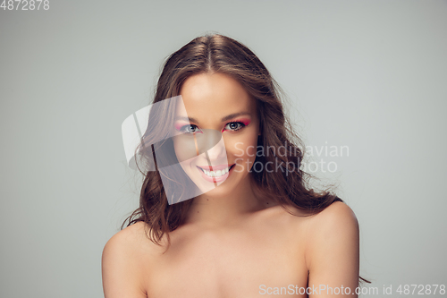 Image of Close up of beautiful young woman with long healthy curly hair and bright make up isolated on grey studio backgroud, smiling with white teeth