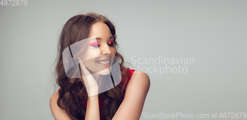 Image of Beautiful young woman with long healthy curly hair and bright make up wearing red dress isolated on grey studio backgroud. Flyer with copyspace.