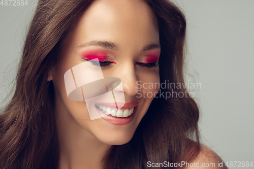 Image of Close up of beautiful young woman with long healthy curly hair and bright make up isolated on grey studio backgroud, shy smiling
