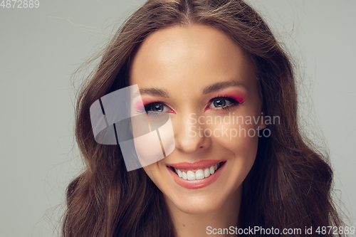 Image of Close up of beautiful young woman with long healthy curly hair and bright make up isolated on grey studio backgroud, smiling with white teeth