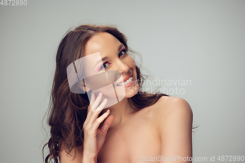 Image of Close up of beautiful young woman with long healthy curly hair and bright make up isolated on grey studio backgroud, smiling with white teeth