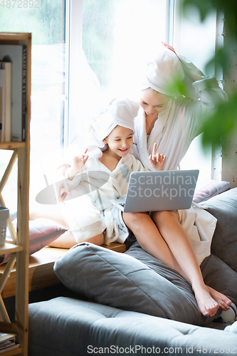 Image of Mother and daughter, sisters have quite, beauty and fun day together at home. Comfort and togetherness. Watching series using laptop near window wearing white bathrobes